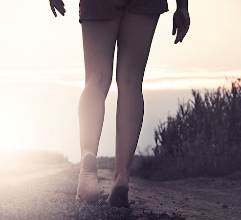 Bare feet walking on a sandy path at sunset